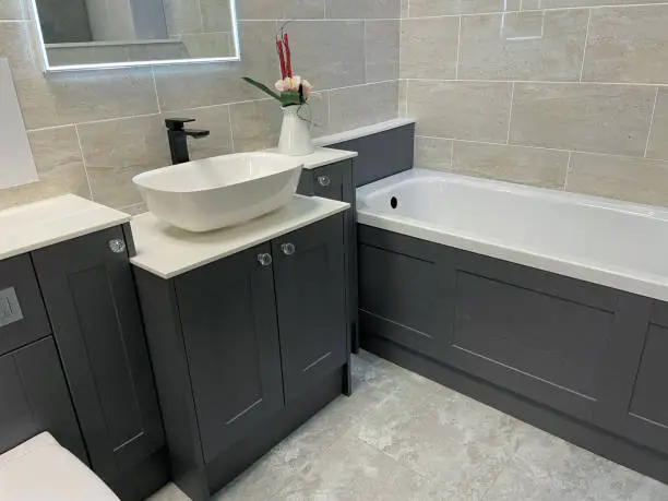 Stock photo showing close-up view of modern, freestanding white sink and black, single lever, monobloc tap over black vanity unit with cream counter top.