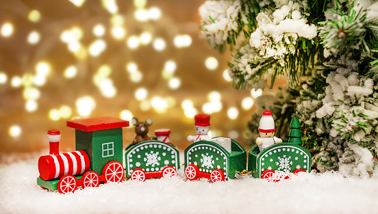 Christmas composition of a train under a Christmas tree with a bokeh on a wooden background with snow