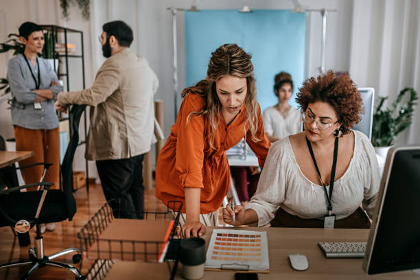 empresária usando computador de mesa com colega olhando para amostra de cores no escritório - heavy labor - fotografias e filmes do acervo