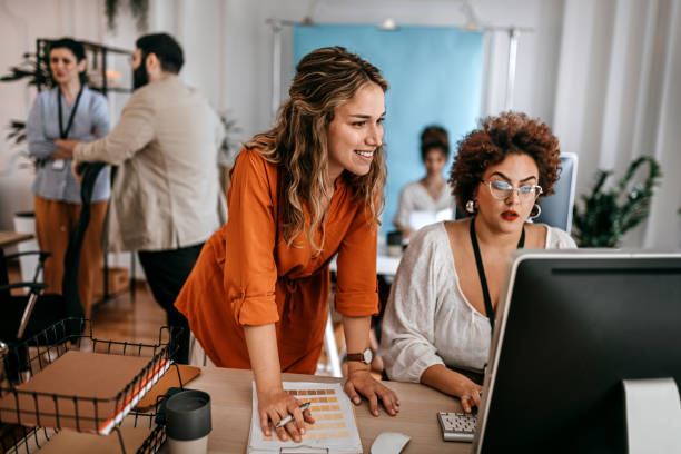 istock Businesswoman using desktop computer with colleague looking at color swatch at office 1349496182