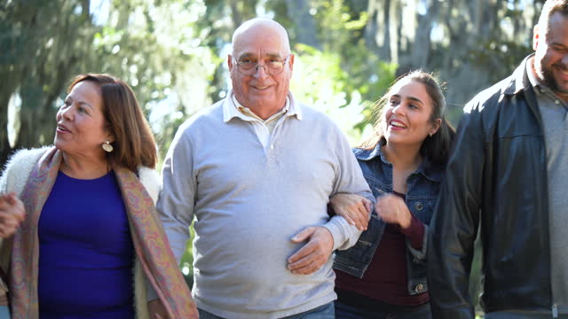 Senior Hispanic couple walk in park with sons, daughters