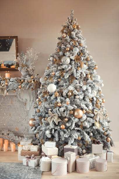 istock Hall room interior with a fireplace with candles and a decorated Christmas tree with presents. Large designer snow tree with lights and balls in beige, gold and silver colors 1349499554
