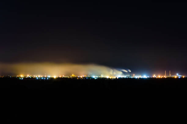 vue sur les lumières de la ville la nuit. la fumée des cheminées de l’usine monte vers le ciel. concept de pollution de l’environnement - factory night skyline sky photos et images de collection