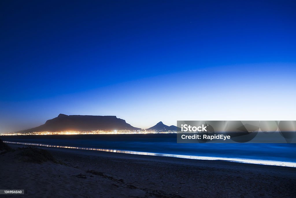 Table Mountain at dusk seen from across bay Atmospheric shot of iconic Table Mountain and Cape Town with twinkling lights, seen in the early evening from Milnerton Beach on the other side of the bay. Shot with Canon EOS 1Ds Mark III.  Africa Stock Photo
