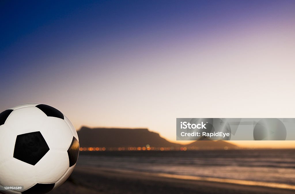 Championship soccer ball at dusk with Table Mountain in background It's 2010 and a championship soccer ball sits on Milnerton beach at twilight with Table Mountain in the background, all ready for the World Cup. Focus is on the ball. Shot with Canon EOS 1Ds Mark III. 2010 Stock Photo