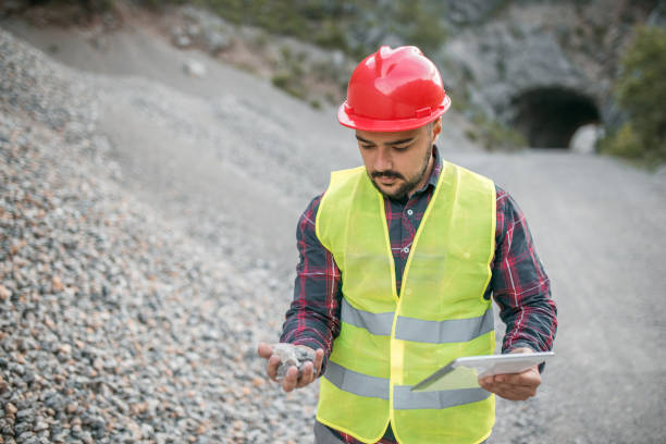 istock Engineer with work helmet in quarry examining a stone he has found and holding digital tablet 1349547928
