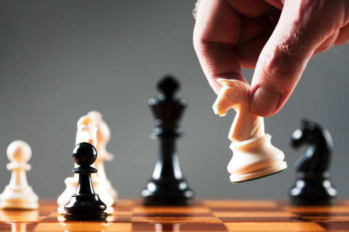 A man's hand takes a white chess knight and prepares to make his move. White knight symbolism, meaning corporate rescue from a takeover by a friendly investor. Shot with Canon EOS 1Ds Mark III.