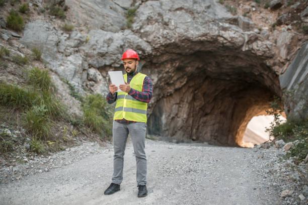 инженер стоит перед туннелем и использует цифровой планшет - construction safety mid adult men road construction стоковые фото и изображения