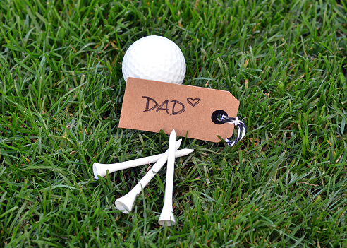 Closeup of a golf ball and golf tees with a note for dad.