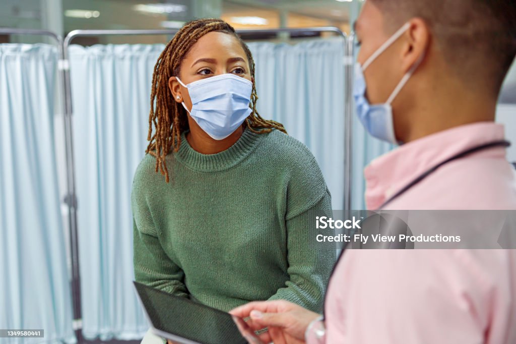 Black woman having medical consultation with doctor A young black woman seeks advice and reviews her medical chart and test results on a tablet computer while in a medical consultation with her male doctor of Asian descent during a routine consultation in a medical clinic. Both individuals are wearing protective face masks to prevent spreading viral infections during the COVID-19 pandemic. Patient Stock Photo