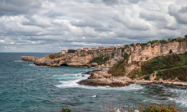 vista delle scogliere che cadono nell'oceano mentre l'acqua turbina intorno alla frastagliata costa rocciosa. formazioni rocciose costeggiano contro il cielo. paesaggio marino con cielo nuvoloso cupo, costa rocciosa - beauty in nature cloud rocky coastline rock foto e immagini stock