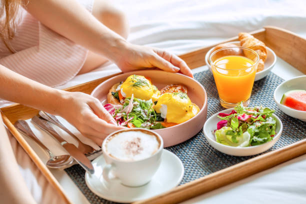 Breakfast in Bed with Coffee, Orange Juice, Salad, Fruits and Eggs Benedict Breakfast in Bed Served with Cup of Coffee, Salad, Fresh Fruits and Eggs Benedict on Wooden Tray. Woman Hands Holding Plate with Fresh Food. Room Service in Hotel room service stock pictures, royalty-free photos & images