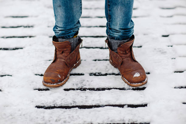 istock Man in blue jeans and old leather boots on snow. Old brown boots covered with snow. 1349600023