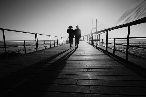 Couple in silhouette walking with the sunrise on their backs.