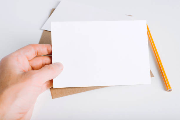 istock Close-up hand showing blank white card mock up template. Craft envelope, pencil and empty postcard template with place for text or branding 1349603507