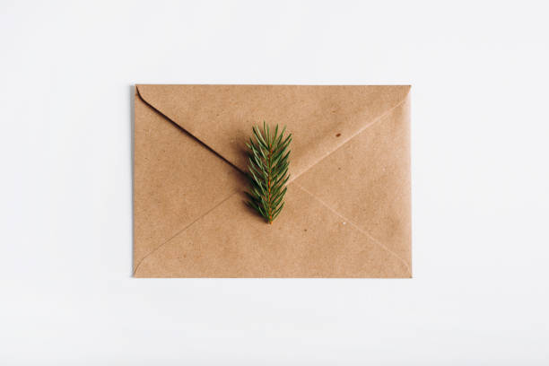 istock Greeting envelope for Christmas or Happy New Year on white table, top view. Closed gift craft envelope for holiday with sprig of pine, flat lay. Festive letter with wishes or congratulations concept 1349603557