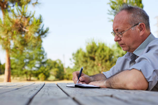 alter mann, der sein testament im park auf einen leeren notizblock schreibt - writing diary nature ideas stock-fotos und bilder