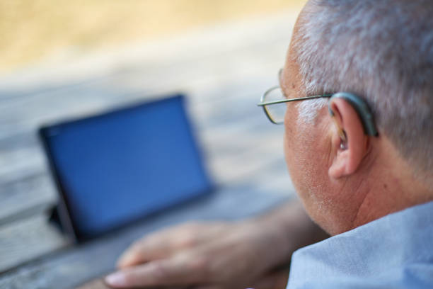 istock selective focus of old man with hearing aid looking tablet outdoor 1349606788