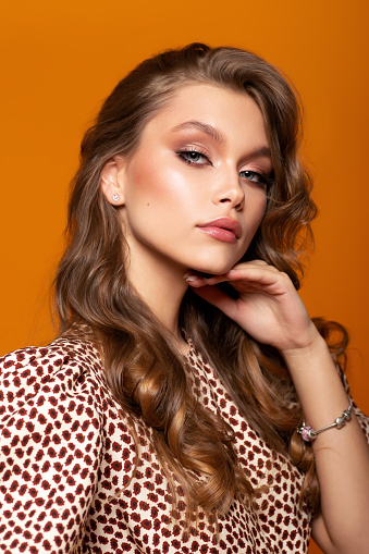 Studio portrait of a chic girl in a dress on an orange background.