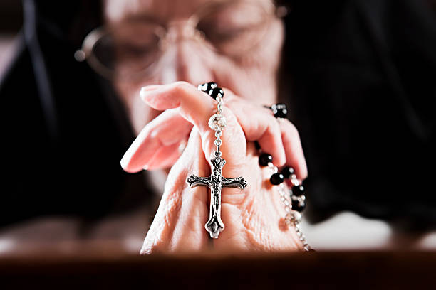 An old nun's hands clasp her rosary as she prays. Eyes closed, a nun prays, hands clasped round her rosary. Focus is on her hands. Shot with Canon EOS 1Ds Mark III. nun praying cross human hand stock pictures, royalty-free photos & images