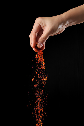 Hand sprinkling cayenne pepper isolated on black background