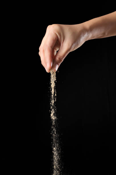 istock Hand sprinkling ground pepper isolated on black background 1349608973