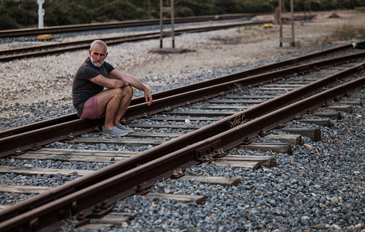 Portrait of adult man sitting on railway track during sunset