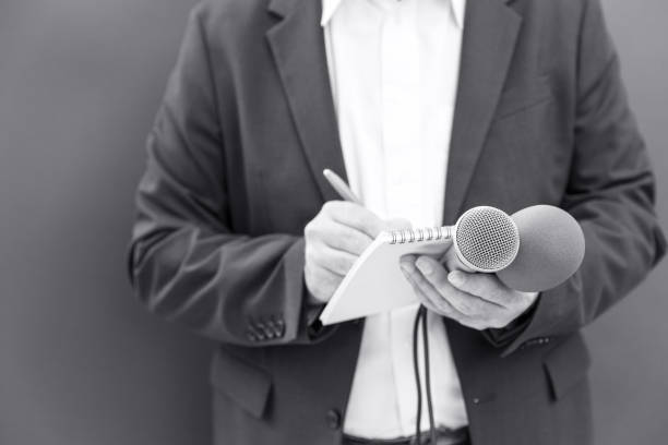 istock News reporter at press conference or media event, holding microphone, writing notes 1349629430