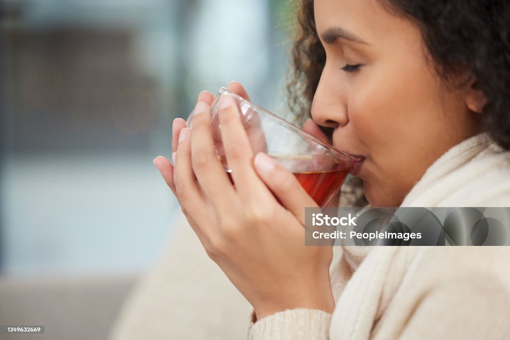 Cropped shot of an attractive young woman drinking a glass of herbal tea while sitting on a sofa at home Detoxing Tea - Hot Drink Stock Photo