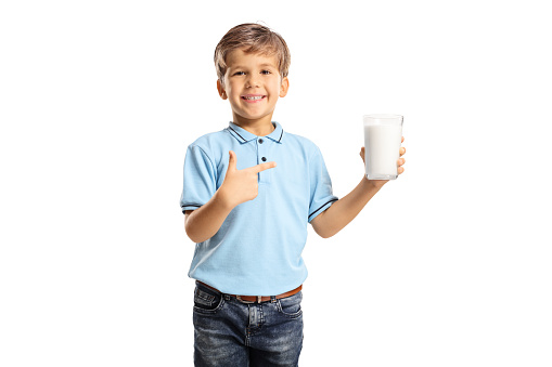 Smiling boy holding a glass of milk and pointing isolated on white background