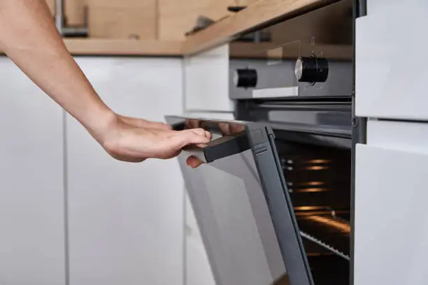 Woman hand open electric oven door with handle. Homemade cooking. Kitchen appliance