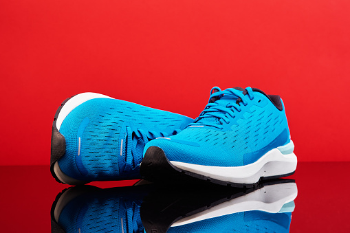 Blue running sneakers on red background. Pair of sport male shoes for fitness with reflection, close up