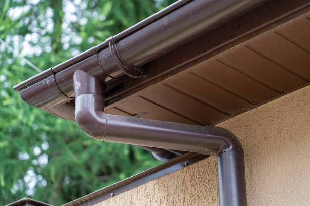 istock Brown plastic gutter system against green trees, roof overhang 1349665681