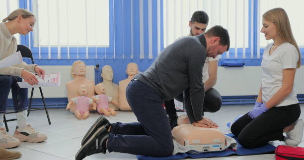 istock Young woman instructor helping to make first aid heart compressions with dummy during the group training indoors. 1349671037