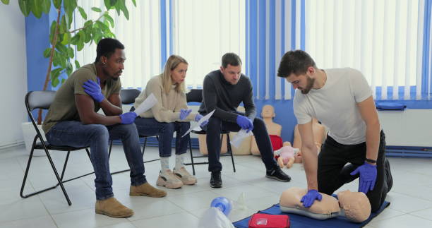 Man instructor showing how to make chest compressions with dummy during the first aid group training indoors.