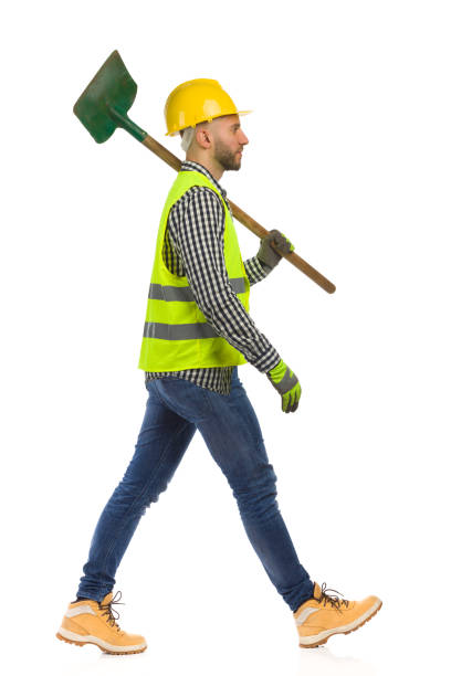 istock Construction worker is walking with shovel on a shoulder. Side view. Studio shot isolated. 1349673106