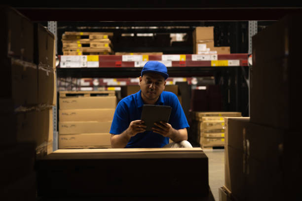 istock Young worker in blue uniform checklist manage parcel box product in warehouse. Asian man employee using tablet working at store industry. Logistic import export concept. 1349679390