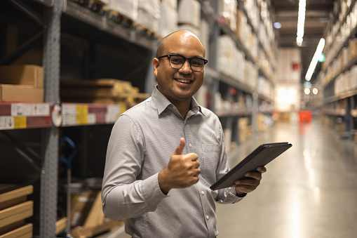 Young manager worker checklist manage parcel box product in warehouse. Asian supervisor man using tablet working at store industry showing thumbs up. Logistic import export concept.