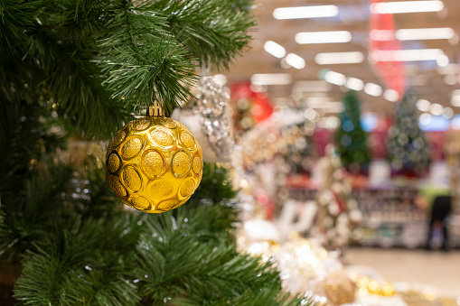 Christmas sale in supermarket, green christmas tree branch with golden ball, blurry store shelves defocused