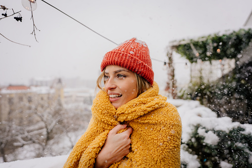Photo of a young woman wrapped in a blanket on the terrace of her loft apartment on a cold snowy day.