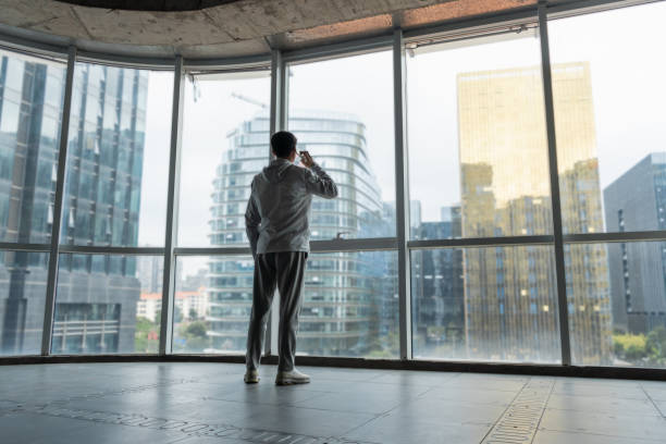 Asian man standing at the window using smartphone