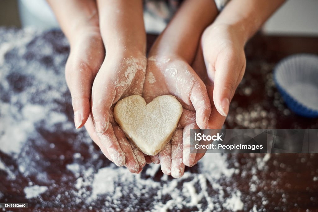 Cropped shot of an unrecognizable girl and her mom holding a heart shaped cookie in the kitchen at home My heart, holding my heart Baking Stock Photo