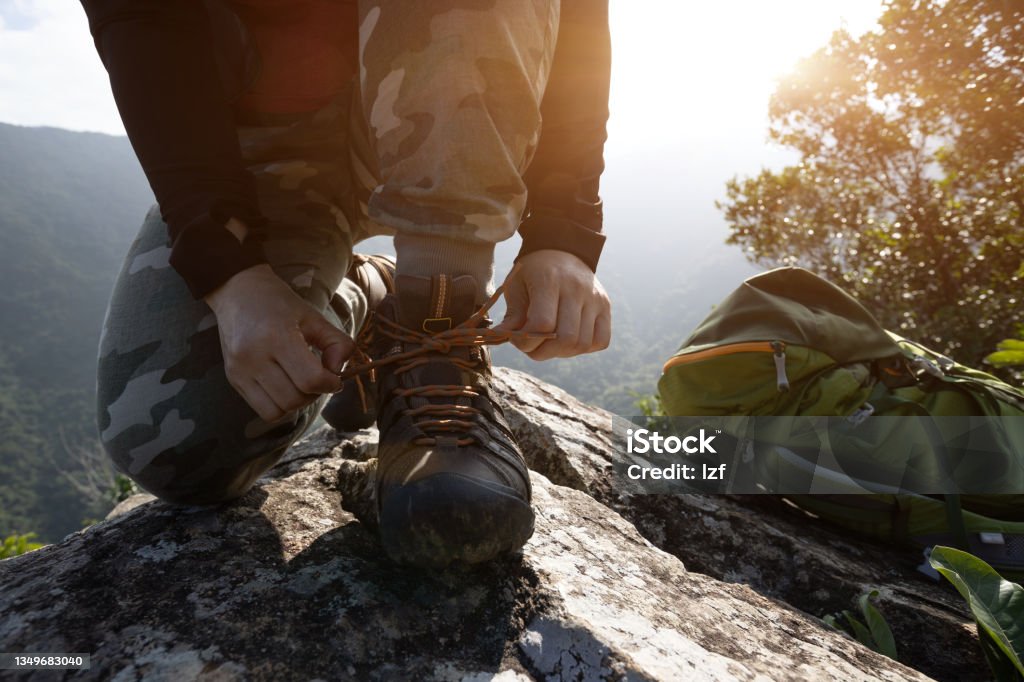 Successful hiker tying shoelace on mountain top cliff edge Sports Shoe Stock Photo