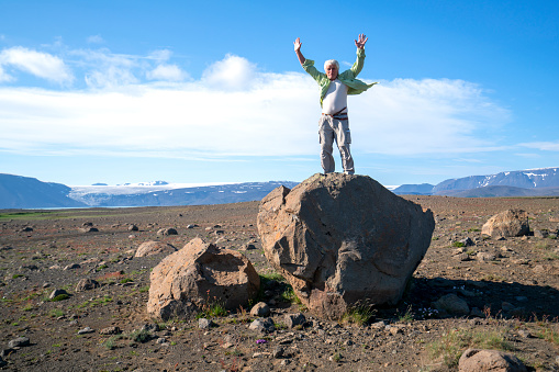 Man on rock, hands up, enjoying Wild Central  Highlands of Iceland with glacier in background.