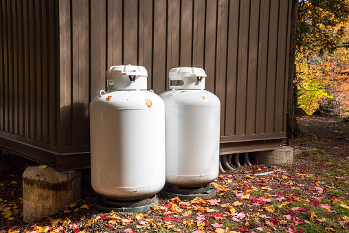 Two white propane tanks at the back of a metal hut in a park in autumn