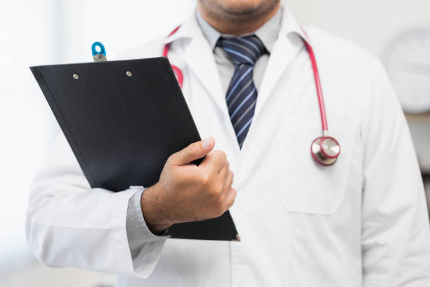 istock Asian doctor standing posing holding clipboard work from home. Positive male physician with stethoscope looking at camera in hospital background. Healthcare and medical concept. 1349688607