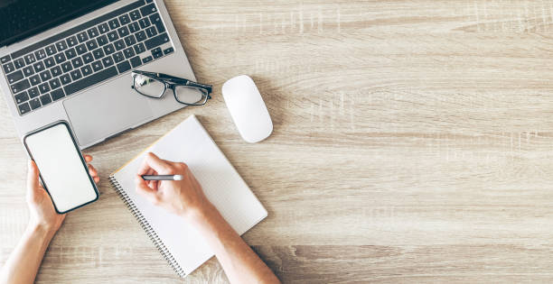 istock Flat lay, top view of desk working space with laptop, hands, notebook and cellphoneFlat lay, top view of desk working space with laptop, hands, notebook and cellphone. 1349688855