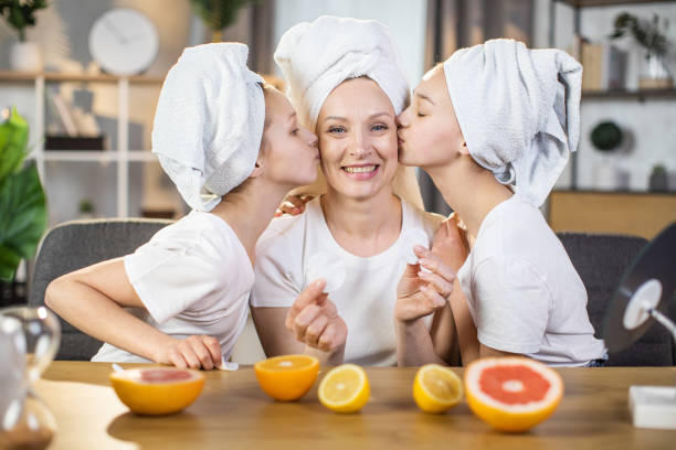 irmãs beijando mãe nas bochechas durante cuidados com a pele em casa - mirror women kissing human face - fotografias e filmes do acervo