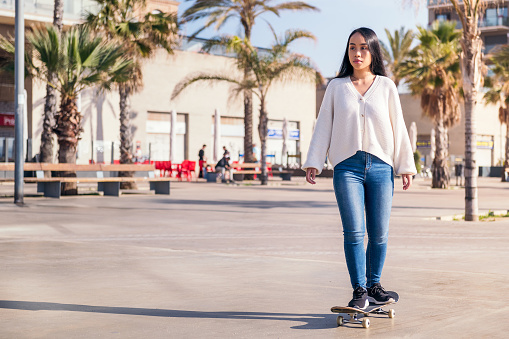 young asian woman riding a skateboard in the city, concept of urban lifestyle