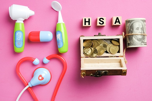 Wooden block written HSA or Healthcare Spending Account with medical toy and covid-19 face mask. One of a number of tax-advantage financial accounts, resulting in payroll tax savings.